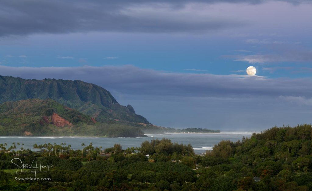 Bay at Hanalei in Kauai with the Na Pali mountain range in the background. Taken just after dawn with the moon setting behind clouds on the horizon