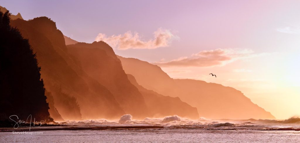 Receding headlands of the Na Pali Kauai coastline illuminated at sunset over a stormy sea with a distant bird. Find prints here in my store