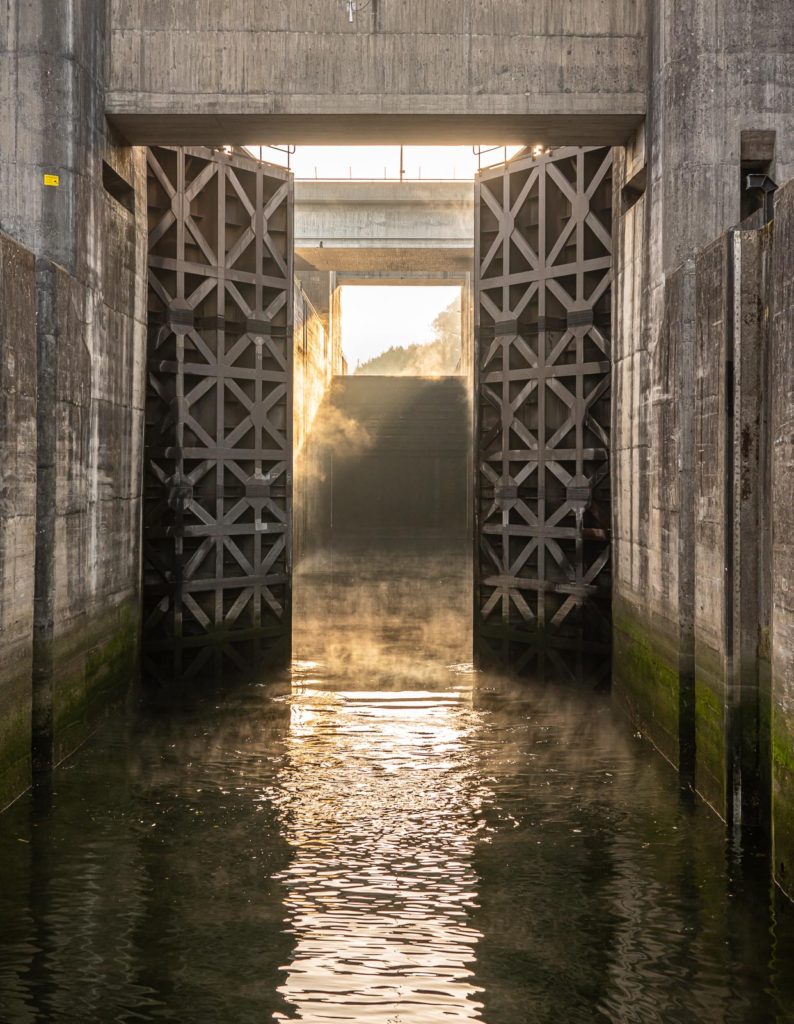 Solid wooden lock gates opening to show the mist from sunrise at the Crestuma Lever dam on River Douro in Portugal
