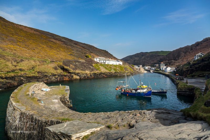 Fishing boats behind harbour wall leading up to old houses and cottages in Boscastle, Cornwall, England, UK