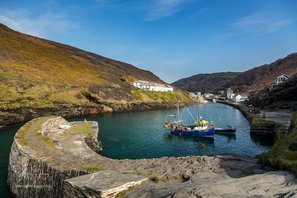 Fishing boats behind harbour wall leading up to old houses and cottages in Boscastle, Cornwall, England, UK. Prints available in my store