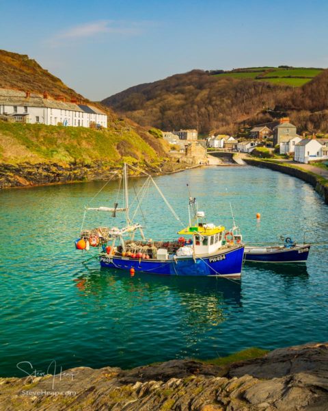 Fishing boats behind harbour wall leading up to old houses and cottages in Boscastle, Cornwall, England, UK