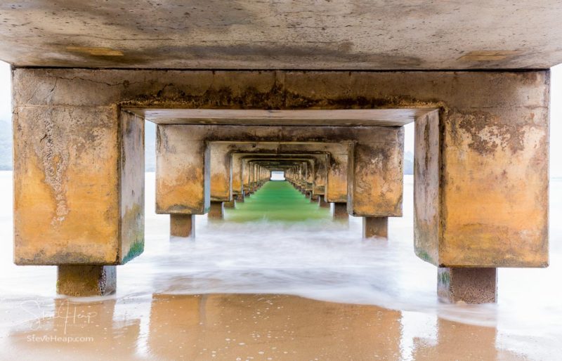 Long exposure blurs ocean and waves underneath Hanalei Pier in Hanalei, Kauai, Hawaii