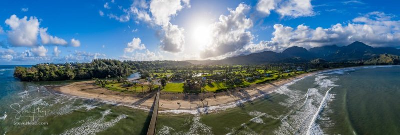 Aerial panoramic image off the coast over Hanalei Bay and pier on Hawaiian island of Kauai as the sun rises over the dramatic landscape