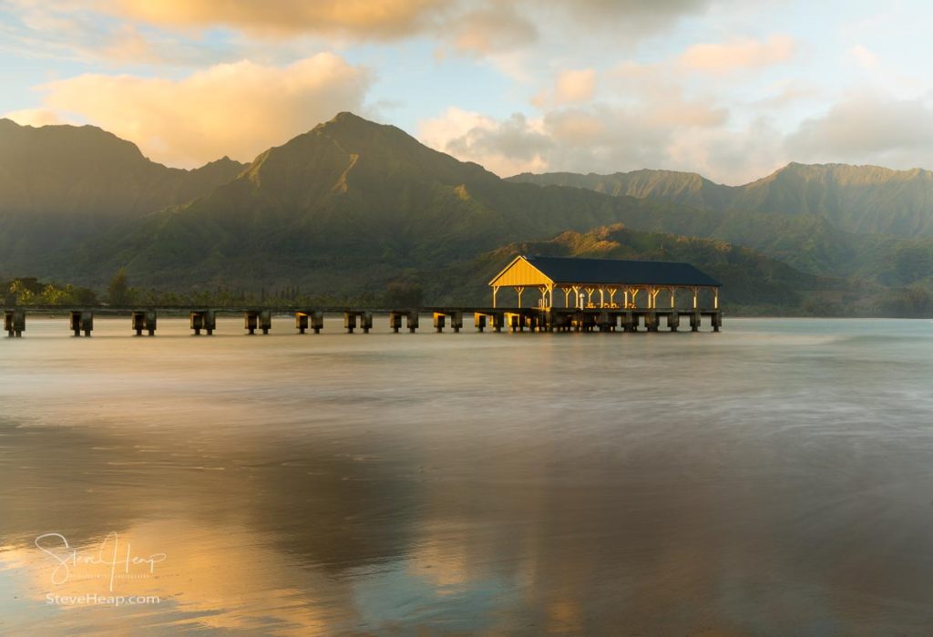 Rising sun illuminates the peaks of Na Pali mountains over the calm bay and Hanalei Pier in long exposure photo. Prints available in my online store