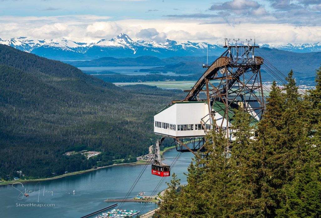 Passengers arriving at the mountain in the red cable car of Goldbelt tram with mountains around Juneau in the distance. Prints available here
