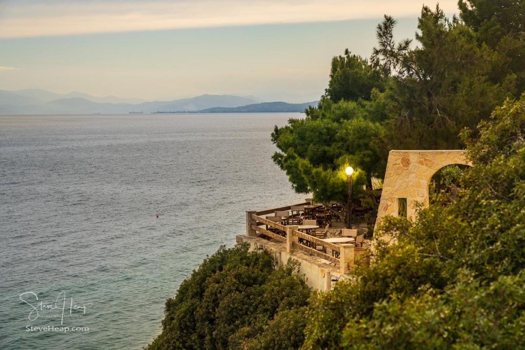 Empty restaurant on stone terrace overlooking ocean from tree covered hill near Athens