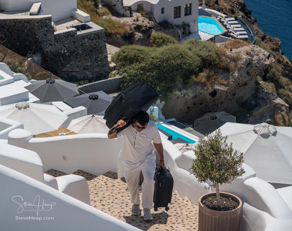 SANTORINI, GREECE - 18 MAY 2019: Hotel porter carries luggage up cliff steps in village of Oia on Santorini