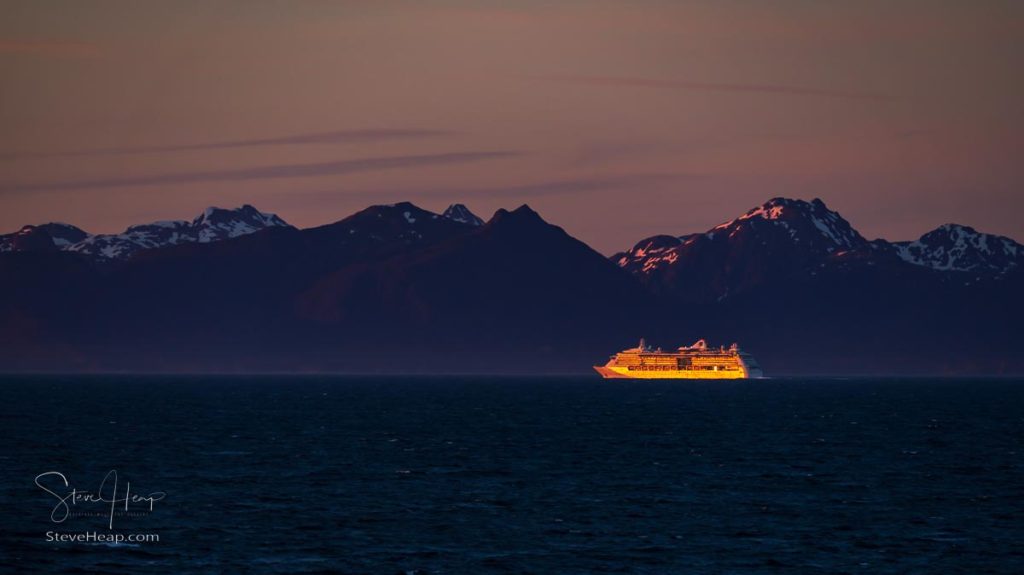 Late evening sunset illuminates a very distant cruise ship against the snowy Alaska coastline