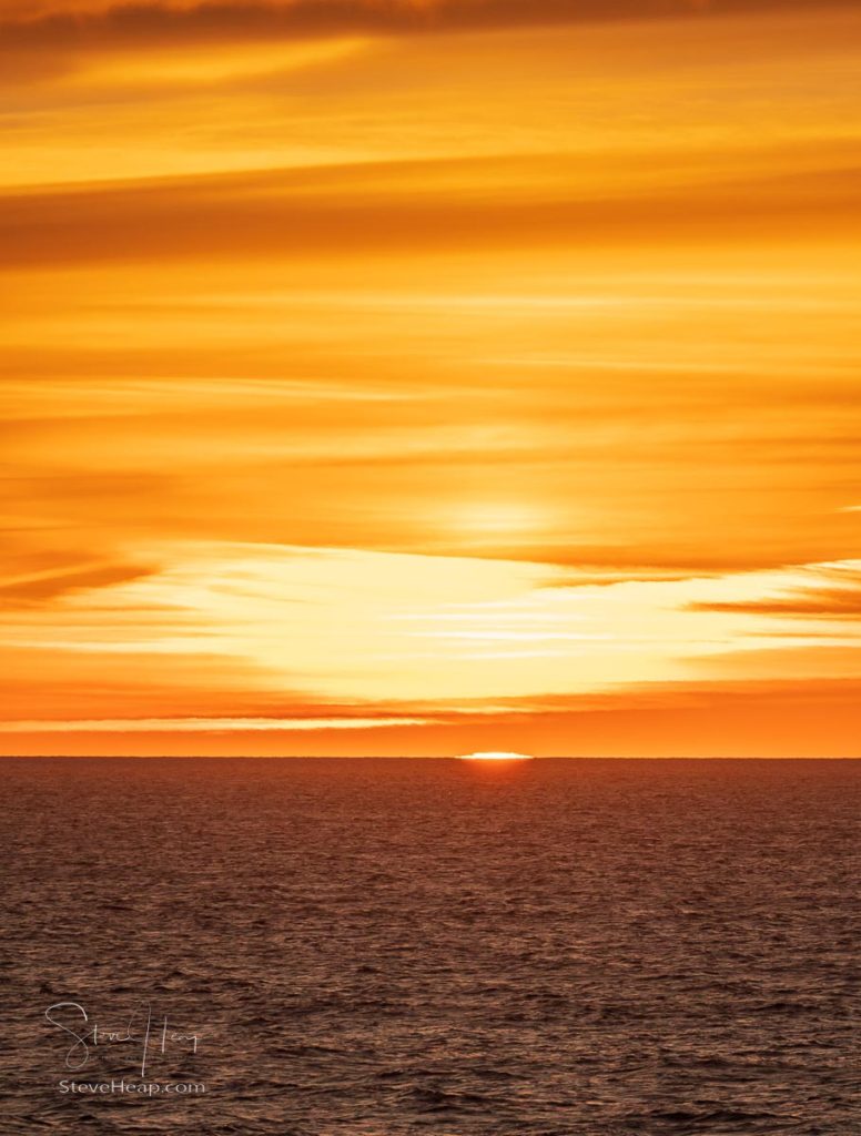 The final section of the sun drops below the water horizon with a colorful sunset over the ocean