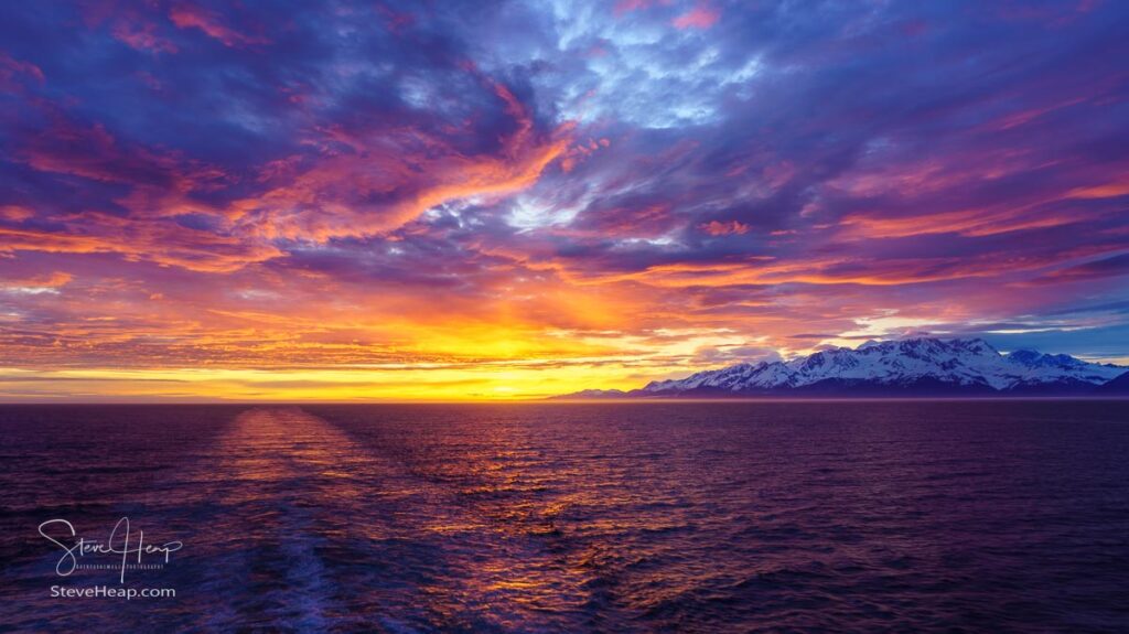 Sun on the horizon by the mountains and Mount Fairweather by Glacier Bay National Park in Alaska. Prints in my online store