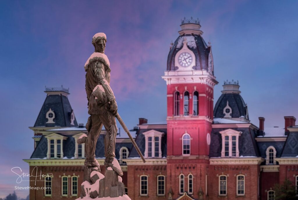 Famous WVU mascot, The Mountaineer, surveys the historic clock tower of Woodburn Hall. A composite of the statue into position in the gardens surrounding the hall to make a perfect graduation gift for a graduating student from the university