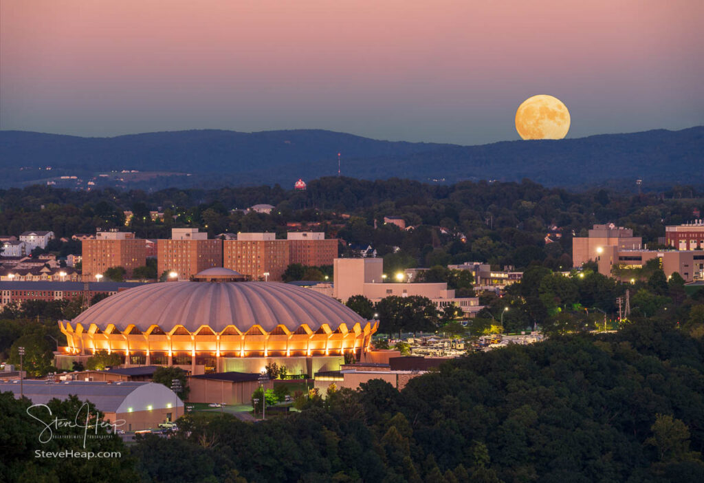Moon rising over the hills surrounding Morgantown with the illuminated Coliseum in the foreground on the Evansdale Campus of WVU