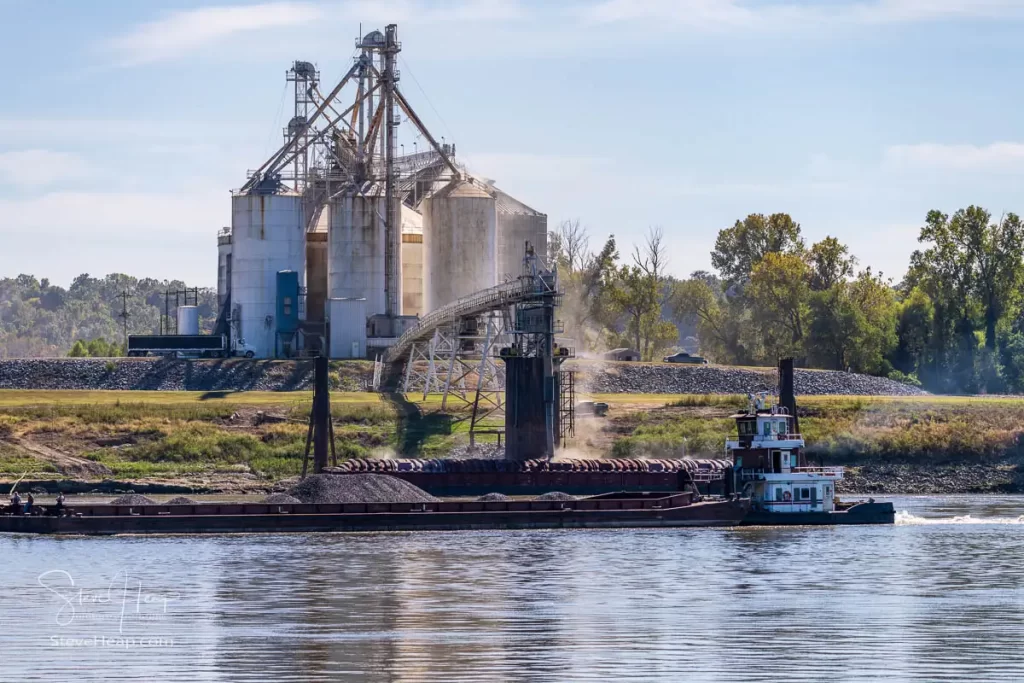 Barges being filled with grain from large grain bins along the riverbanks