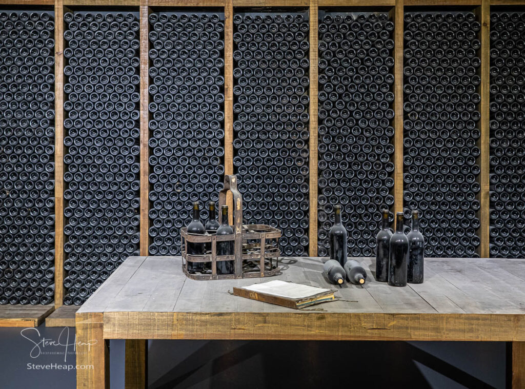 Stacks of wine bottles laying flat in wooden racks in old wine cellar or cave with tasting table at the Sandeman estate