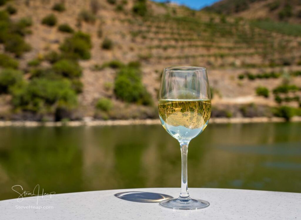 Glass of white wine on the deck of cruise boat on the river in the Douro valley in Portugal reflecting the terraced vineyards on the hillsides