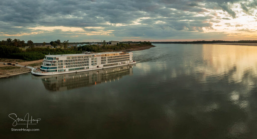 Vicksburg, MS - 25 October 2023: Viking Mississippi docked by bank as sunset cast golden glow on the boat and reflections