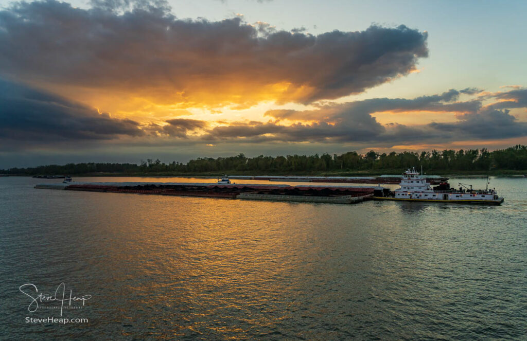 Dramatic sunset over river barge carrying coal down the Mississippi river in Baton Rouge Louisiana looking towards Port Allen