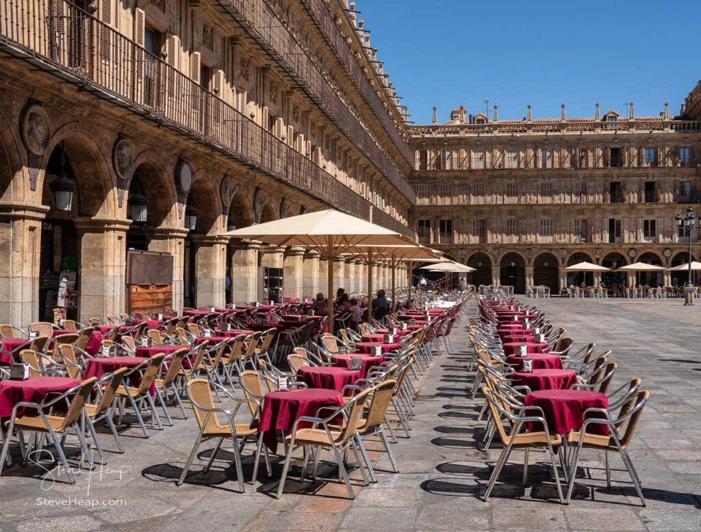 Tables and chairs of outdoor cafe in Plaza Mayor in Salamanca with just a few people having a morning coffee