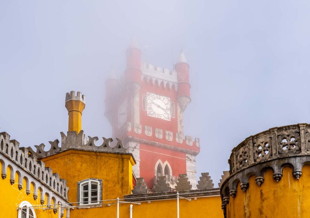 Low clouds and mist hide the colorful and dramatic towers of Pena Palace on the hills above Sintra in Portugal