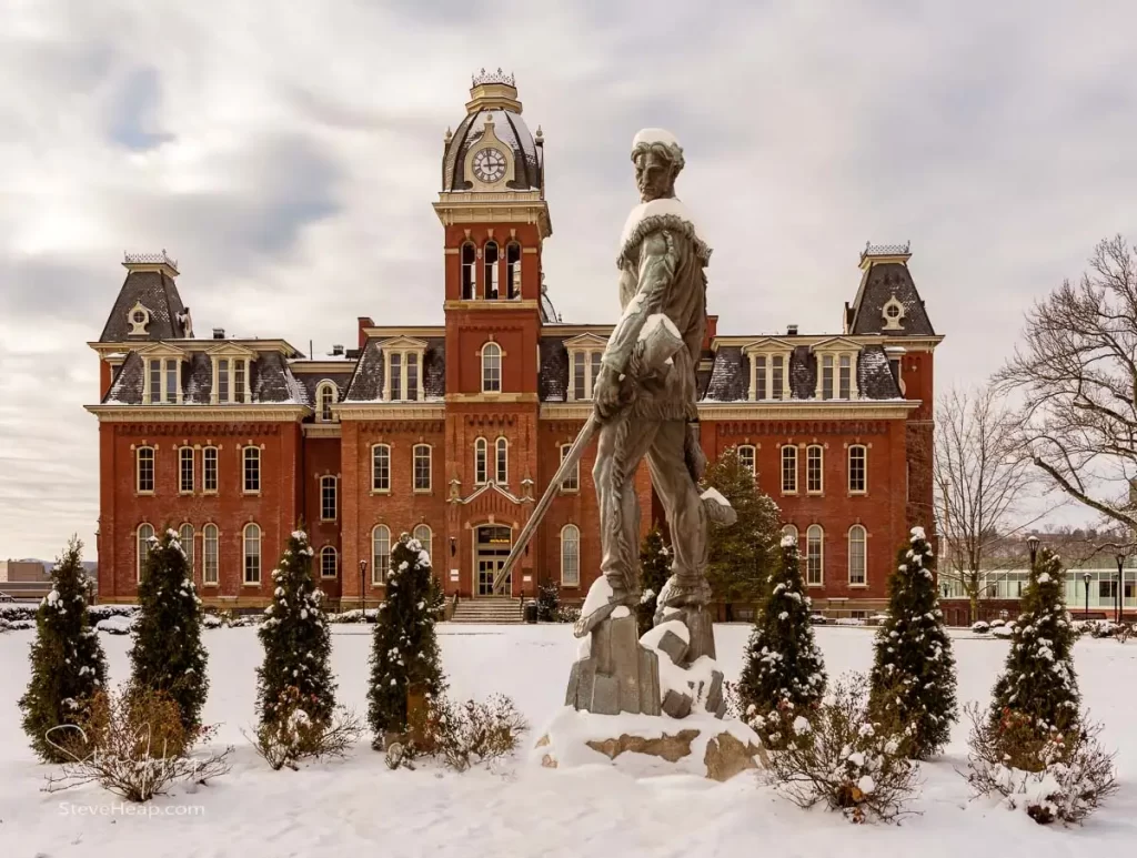 Famous WVU mascot The Mountaineer surveys the historic Woodburn Hall. A composite of the statue into position in the gardens surrounding the hall to make a perfect graduation gift for a graduating student from the university