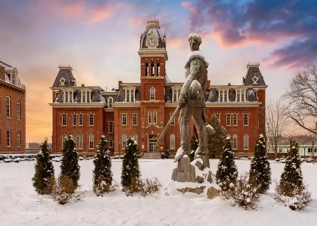 Famous WVU mascot The Mountaineer surveys the historic Woodburn Hall. A composite of the statue into position in the gardens surrounding the hall to make a perfect graduation gift for a graduating student from the university