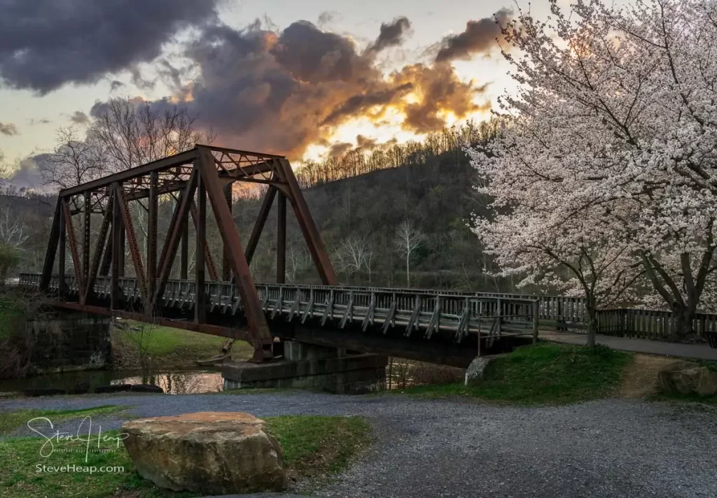 Old steel girder bridge carrying walking and cycling trail in Morgantown WV over Deckers Creek with cherry blossoms blooming in the spring