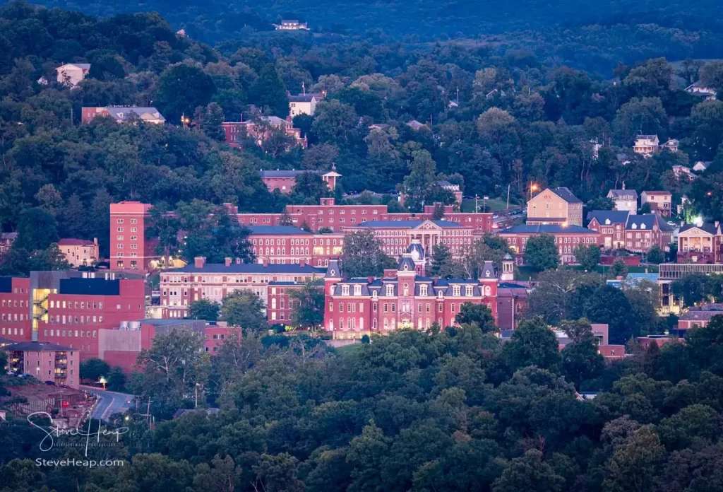 Downtown campus of West Virginia university and Woodburn hall as setting sun gives a warm glow to Morgantown WV. Experience the timeless beauty of West Virginia University's downtown campus at night with this captivating wall art print. Bathed in the warm glow of floodlights and street lamps, the iconic Woodburn Hall stands tall amidst the city's nocturnal skyline.