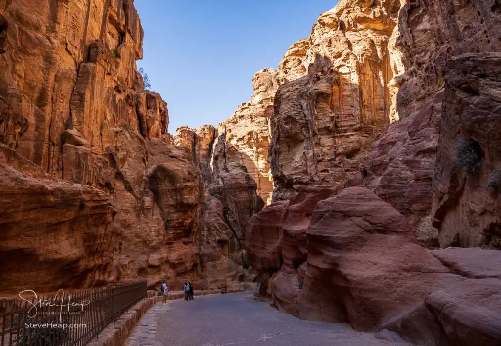 Tourists admiring the rock formations in narrow gorge of the Siq entering Petra