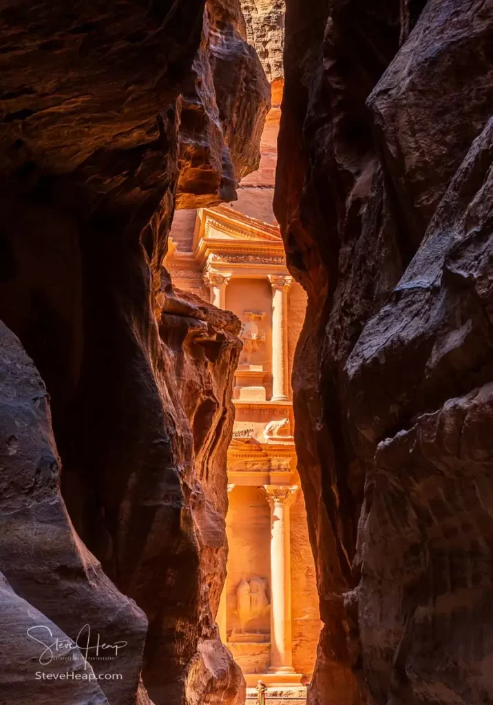 The carved facade of the Treasury building or Al-Khazneh in the ancient city of Petra in Jordan seen through narrow Siq gorge