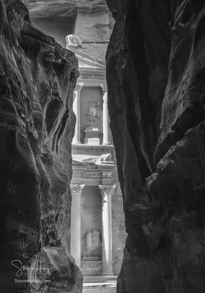 The carved facade of the Treasury building or Al-Khazneh in the ancient city of Petra in Jordan seen through narrow Siq gorge in monochrome