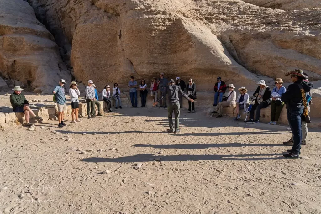 Tour group gathering in a shaded area in Petra, listening to a guide share insights about the site's history.