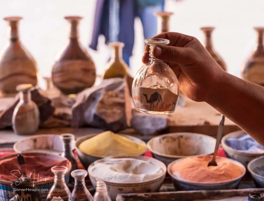 Making sand art in bottles with a camel in the desert