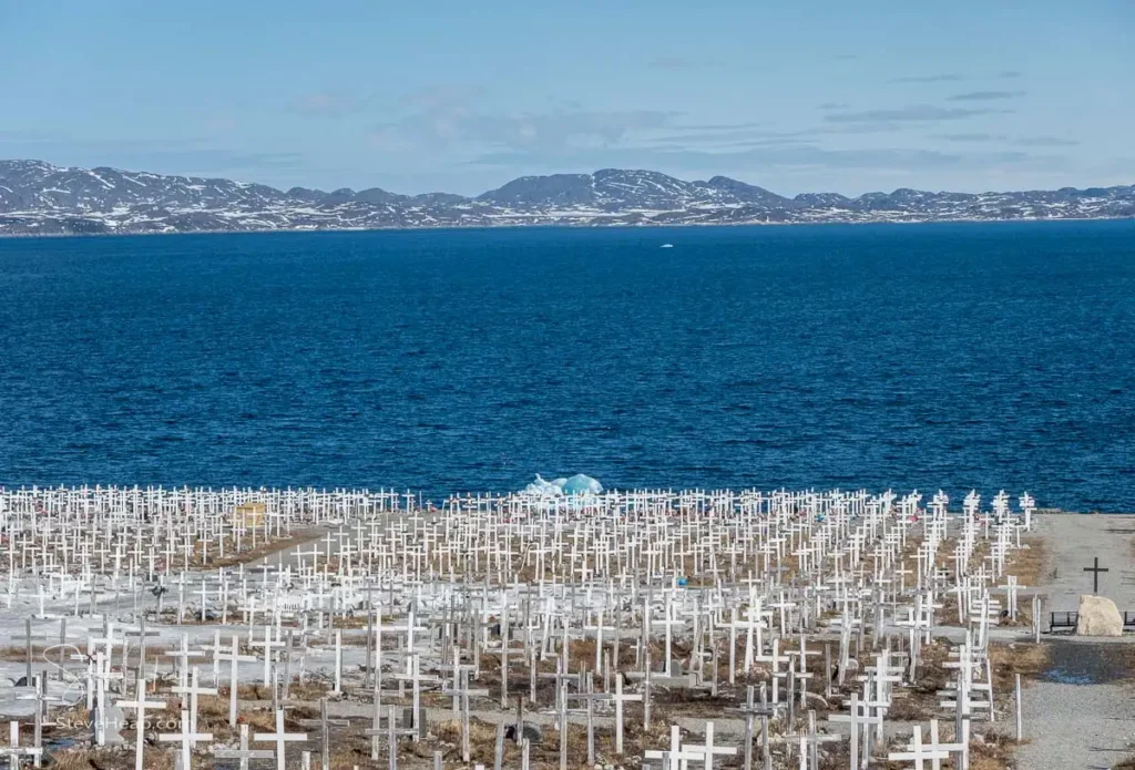 Rows of crosses for graves in old historic cemetery off Siaqqinneq in Nuuk in Greenland with iceberg in Fjord