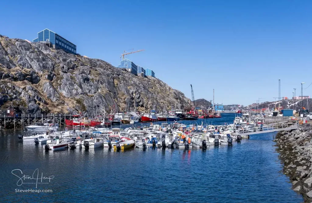The interior of Nuuk harbour in Greenland with many small power boats and larger fishing trawlers docked in rocky fjord