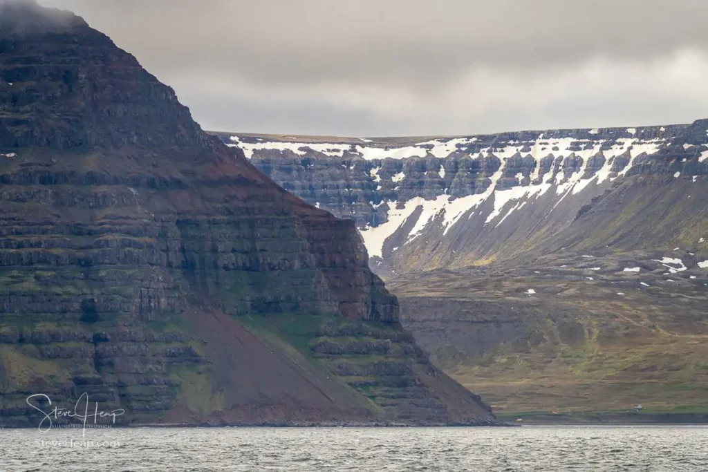Dramatic landscape view of mountains and sea in Iceland, near Isafjordur, under an overcast sky with small homes on the coastline
