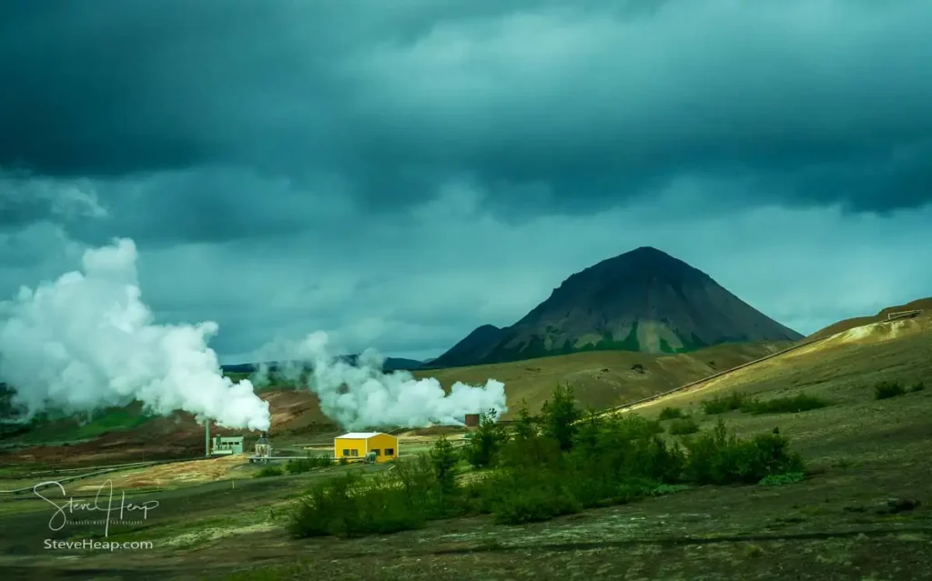 Steam rises from geothermal power stations in a dramatic landscape dominated by volcanic mountains in Iceland's northern environment