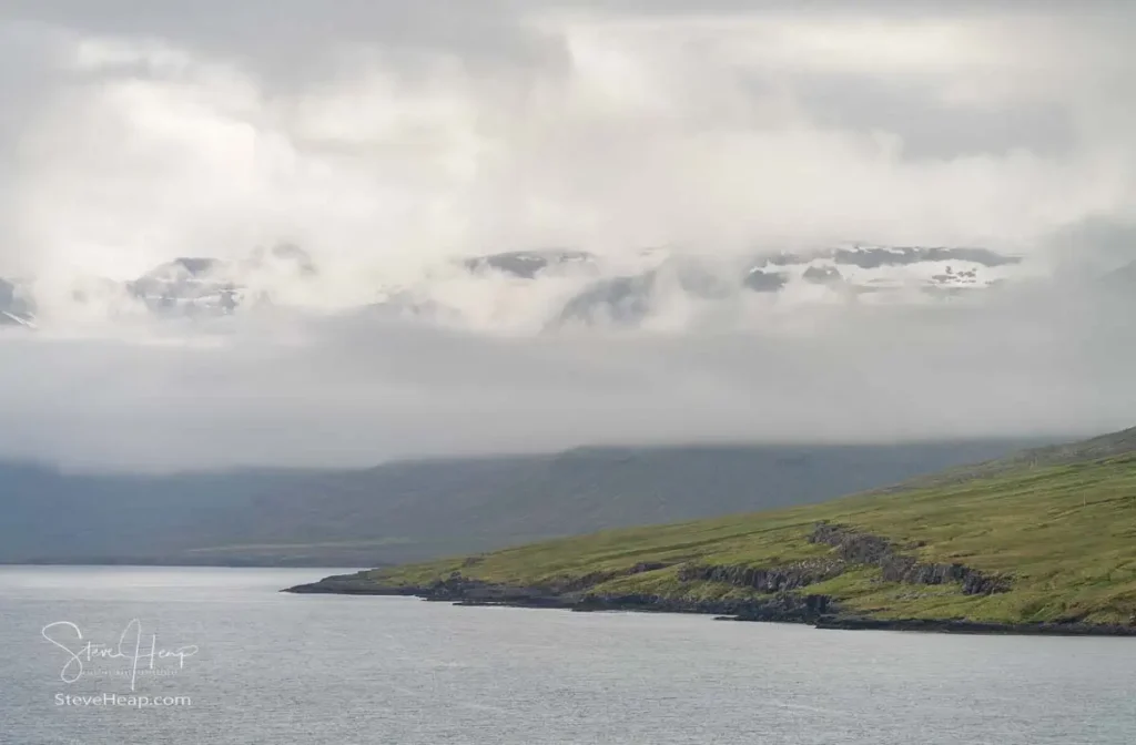 Low clouds over the mountains approaching Seydisfjordur in the East of Iceland with the snow capped peaks appearing through the clouds