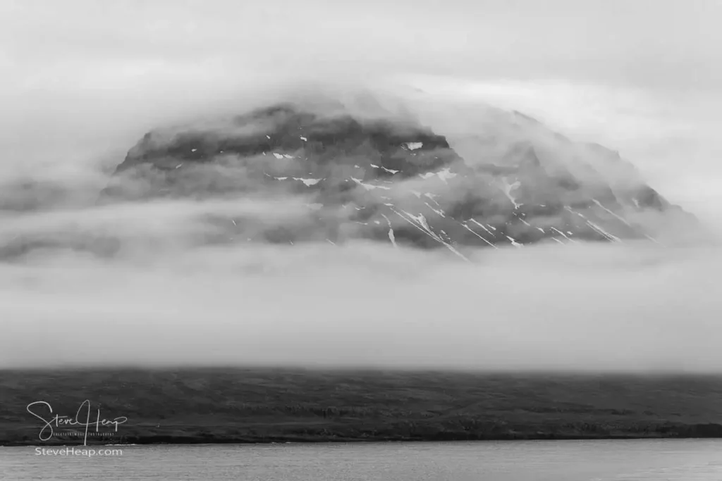 Snow flecked mountain appears through the clouds as we sail away from Seydisfjordur in Iceland