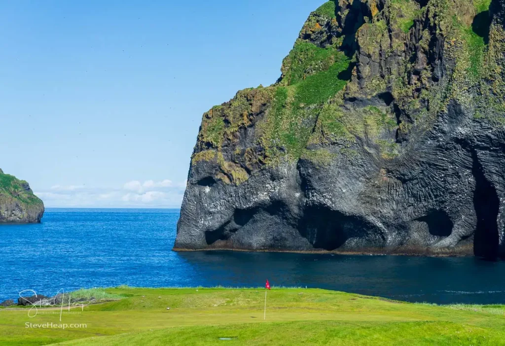 View across the golf course to the rocky shoreline of Heimaey Island in Iceland with elephant head shaped rock