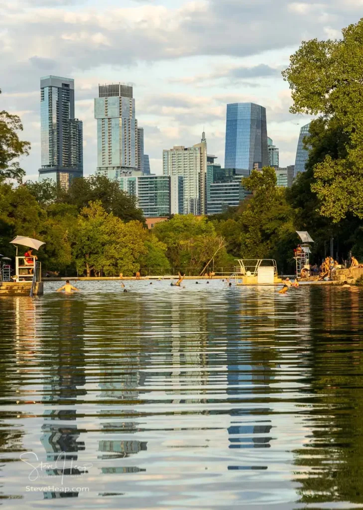 Swimmers in the Barton Springs swimming pool with Austin skyline at sunset