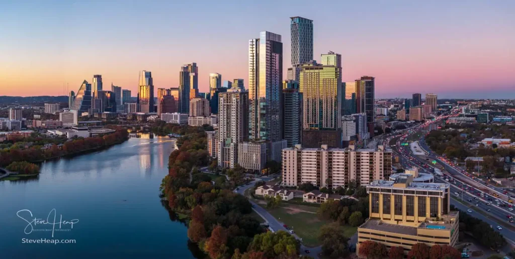 A wide aerial view of the transformed 2026 Austin, Texas skyline. The crane-free downtown area is visible behind the new luxury high-rises of the Rainey Street development, situated along the waters of Lady Bird Lake.