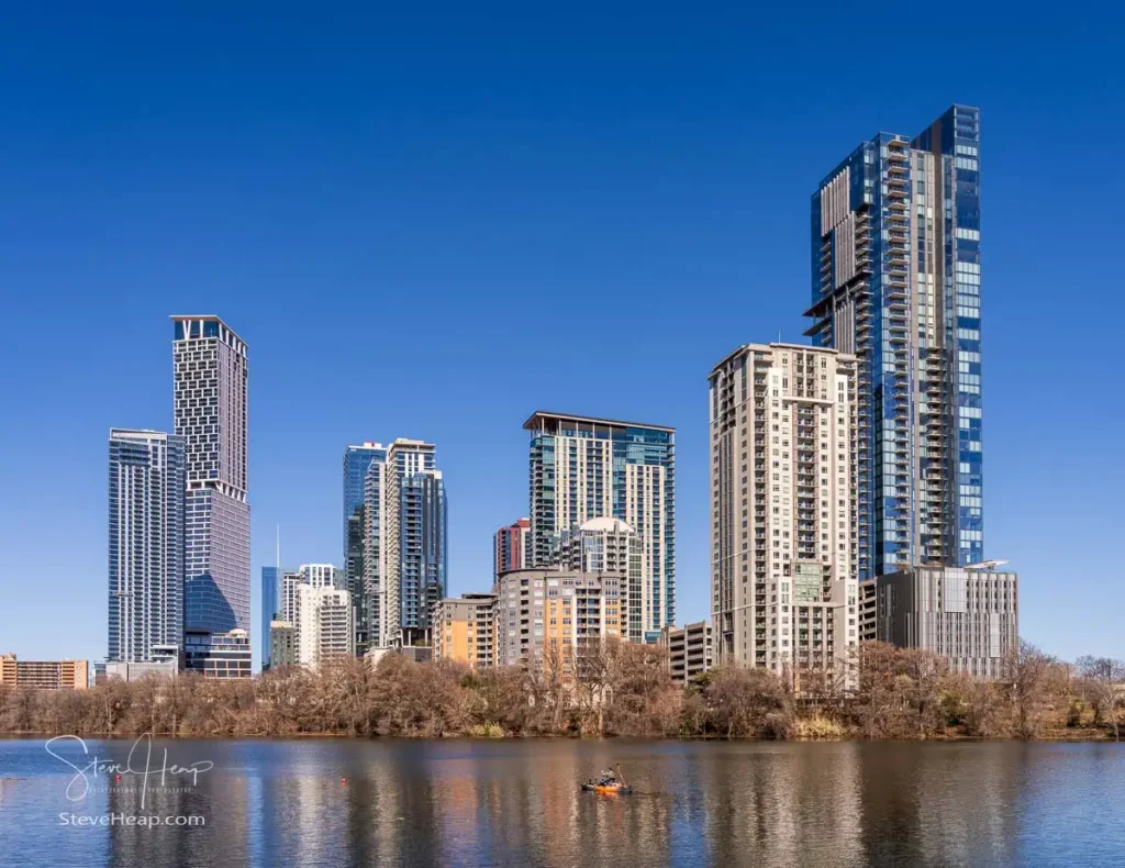 A ground-level view from across Lady Bird Lake during winter, highlighting the completed modern architecture of the Rainey Street District in downtown Austin, Texas. Ideal as high-quality landscape wall decor