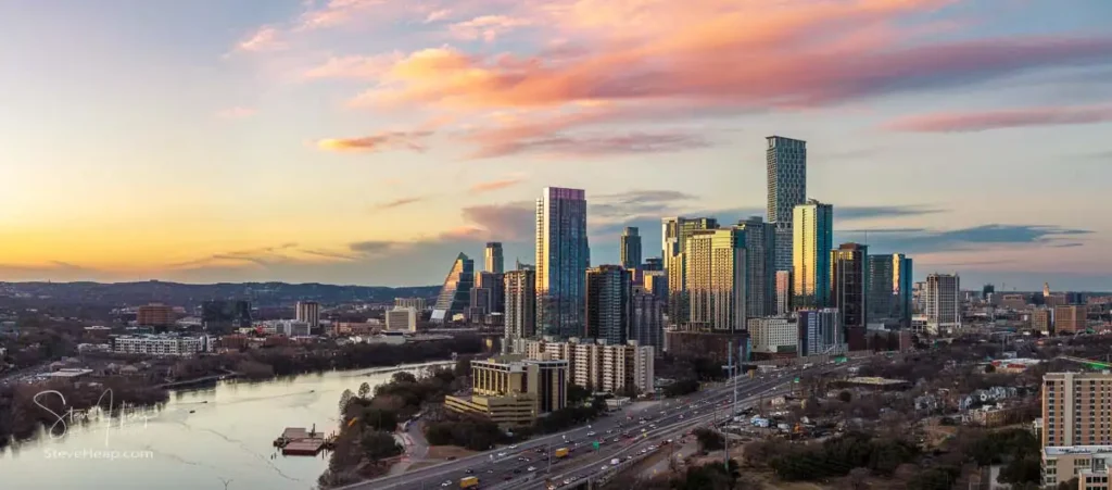 A dramatic sunset panorama of the crane-free Austin skyline in 2026. Vibrant clouds sit behind the city's newest and tallest skyscrapers, viewed from the east over the Colorado River and I-35 traffic.