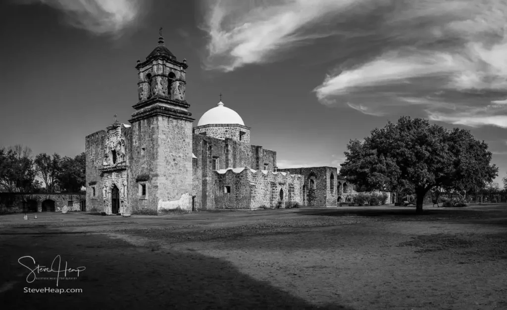 Distant black and white wide shot showing the immense scale and isolation of the San Jose mission facade in an empty plaza