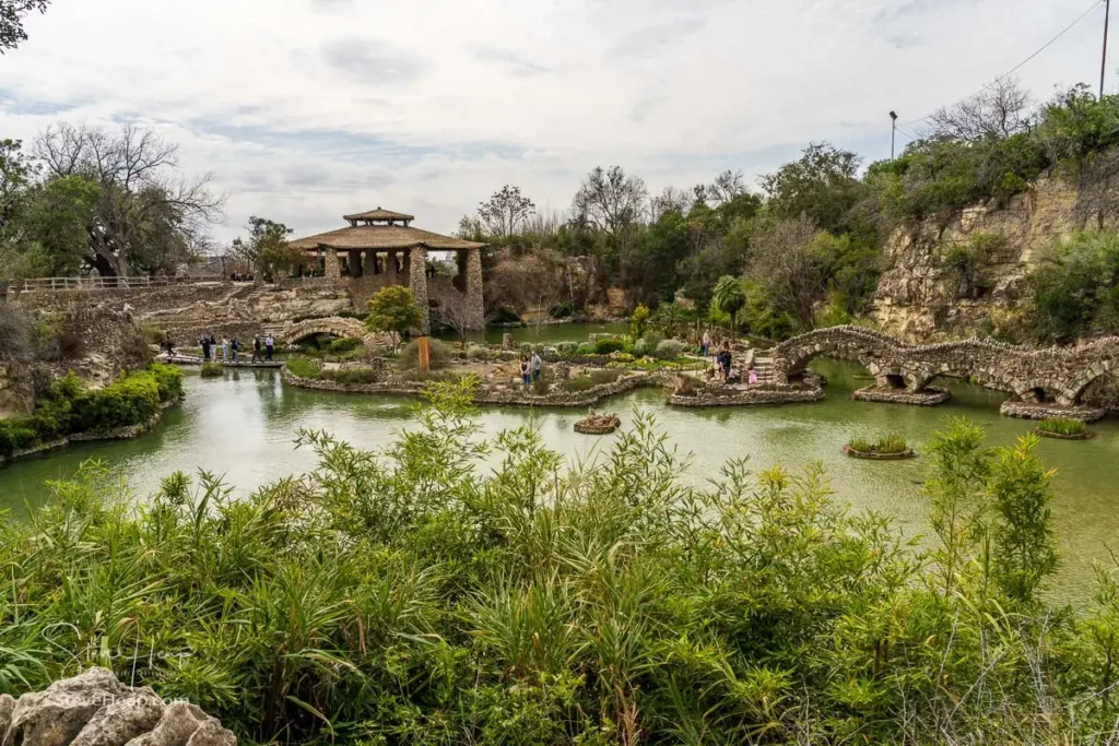 Tranquil pond with a stone bridge and lush green foliage reflecting in the water at the San Antonio Japanese Tea Garden.