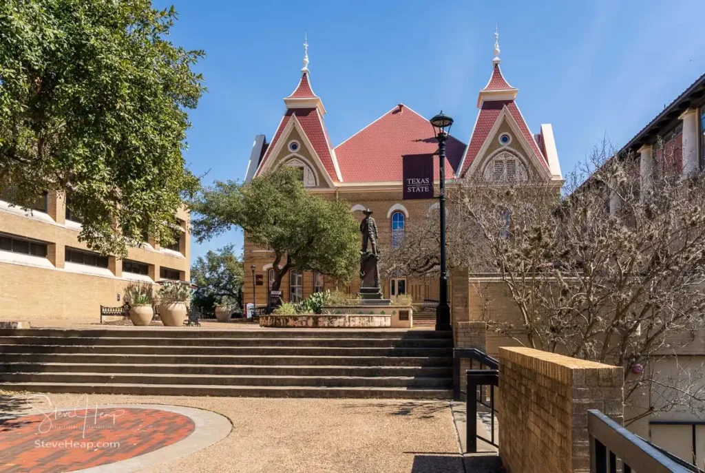 Sunlit exterior of the historic Old Main building featuring distinctive red spires on the Texas State University campus in San Marcos