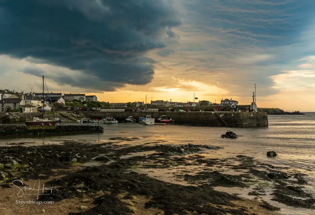Moody sunset over Cemaes harbor with docked boats under heavy Welsh storm clouds